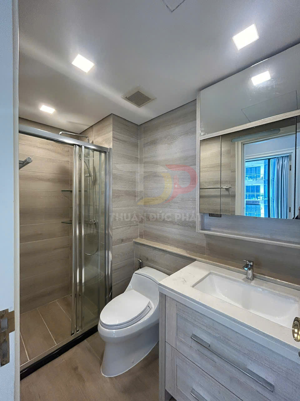 Phòng tắm hiện đại với bồn cầu, buồng tắm kính và lavabo tủ gỗ sáng màu