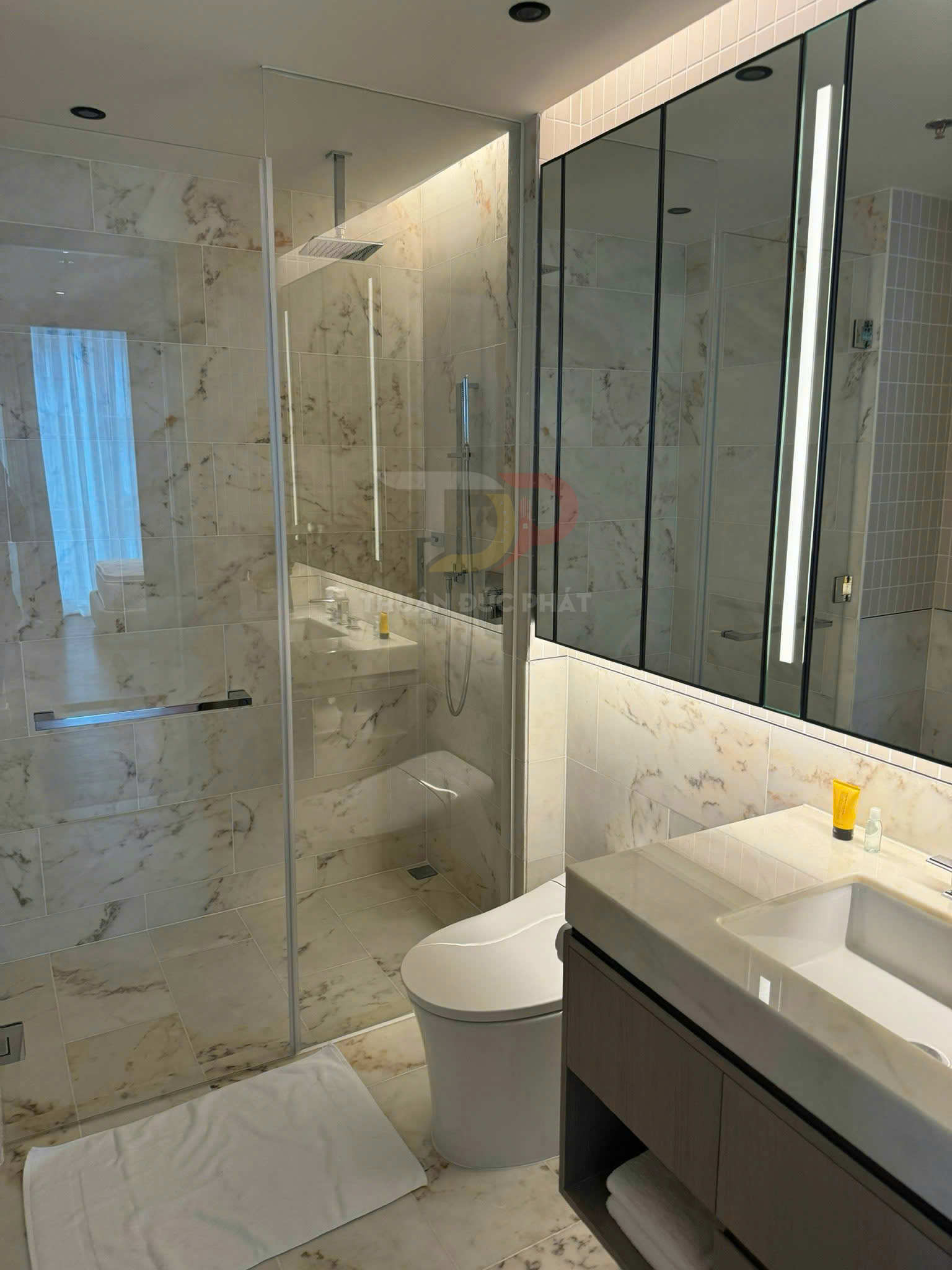 Phòng tắm hiện đại với bồn cầu, buồng tắm kính, lavabo đá marble và gương lớn có đèn LED