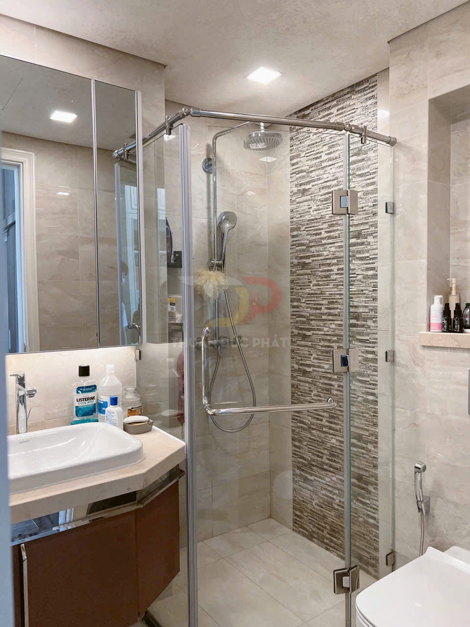 Phòng tắm hiện đại với buồng tắm kính góc, vòi sen treo tường và lavabo cạnh gương lớn