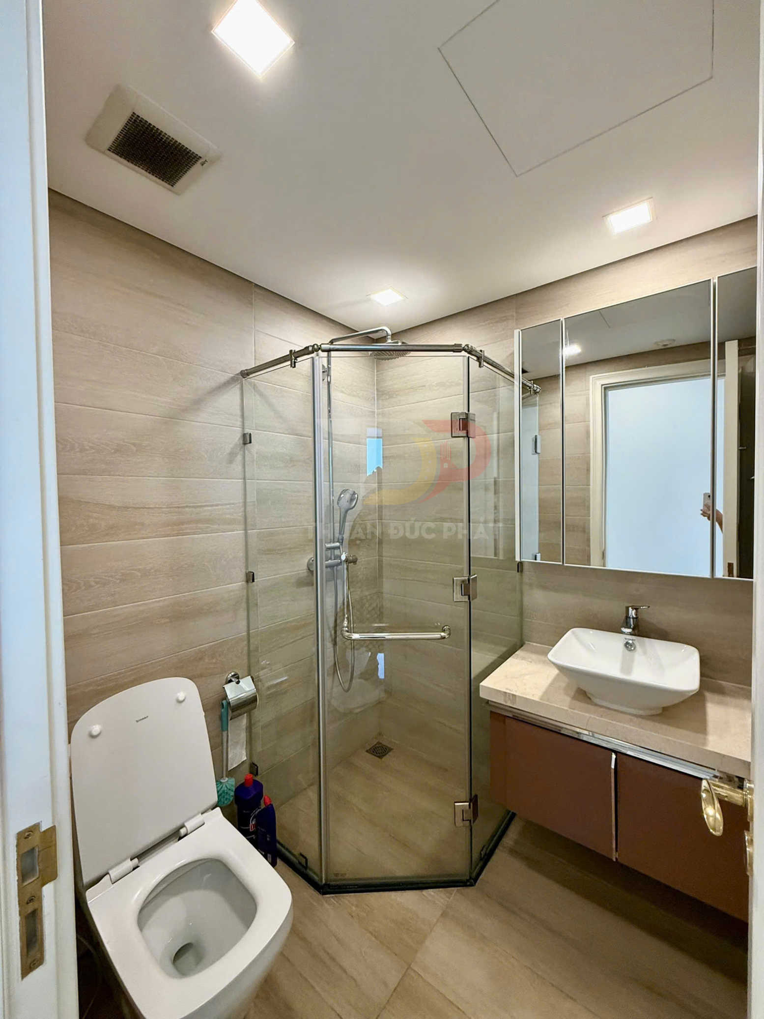 Phòng tắm hiện đại với buồng tắm kính, bồn cầu và lavabo đặt trên tủ gỗ gắn tường