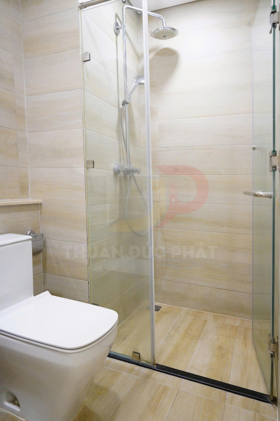 Phòng tắm kính hiện đại với buồng tắm đứng và bồn cầu sứ trắng trên nền gạch giả gỗ