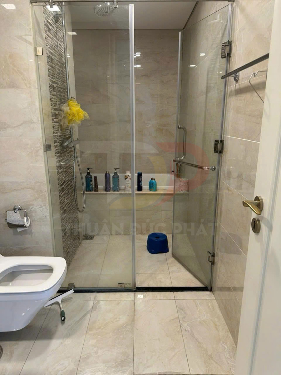 Phòng tắm kính hiện đại với buồng tắm đứng, vòi sen, kệ để sữa tắm và bồn cầu treo tường