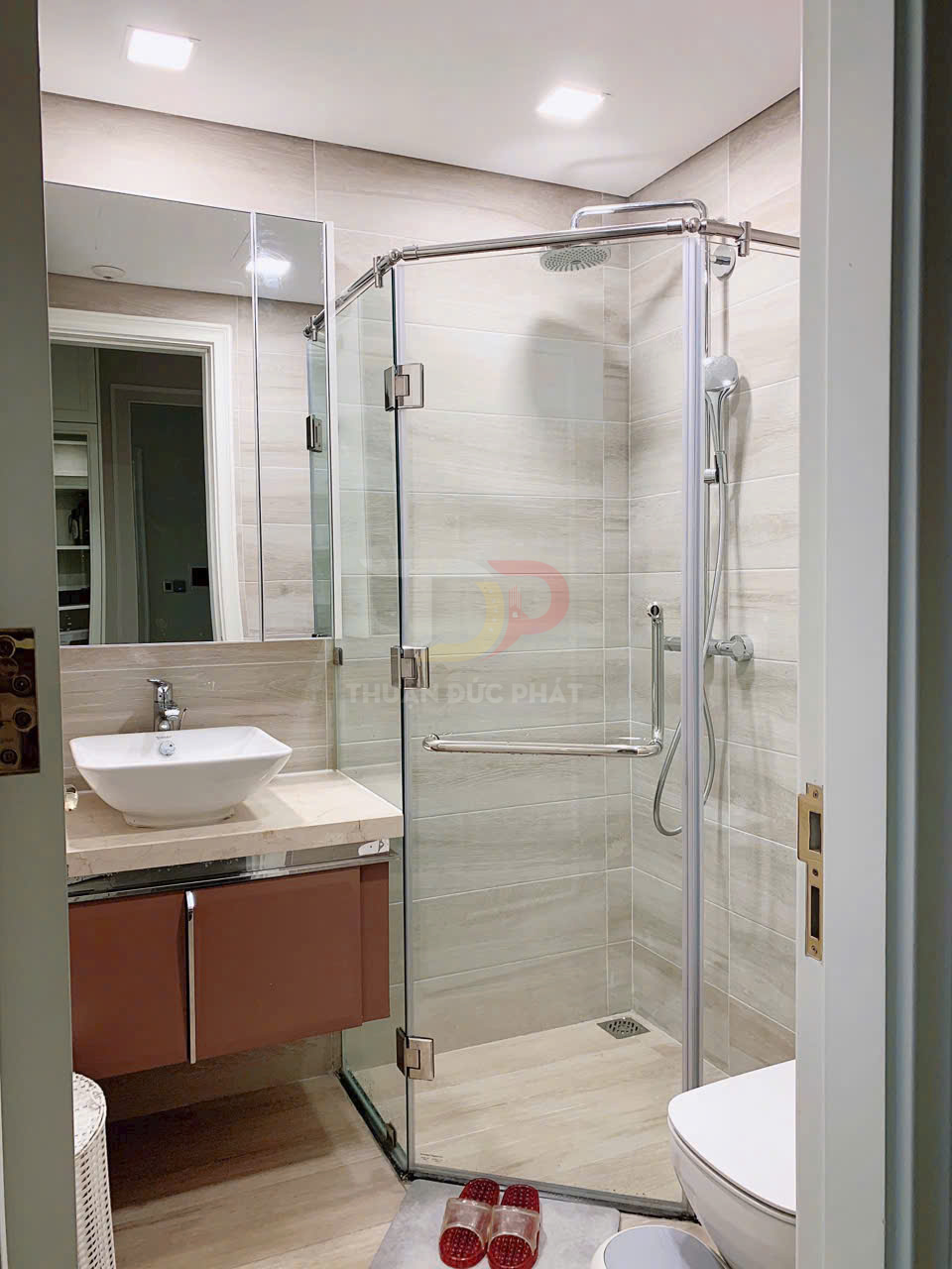 Phòng tắm hiện đại với buồng tắm kính góc, vòi sen treo tường và lavabo đặt trên tủ gỗ