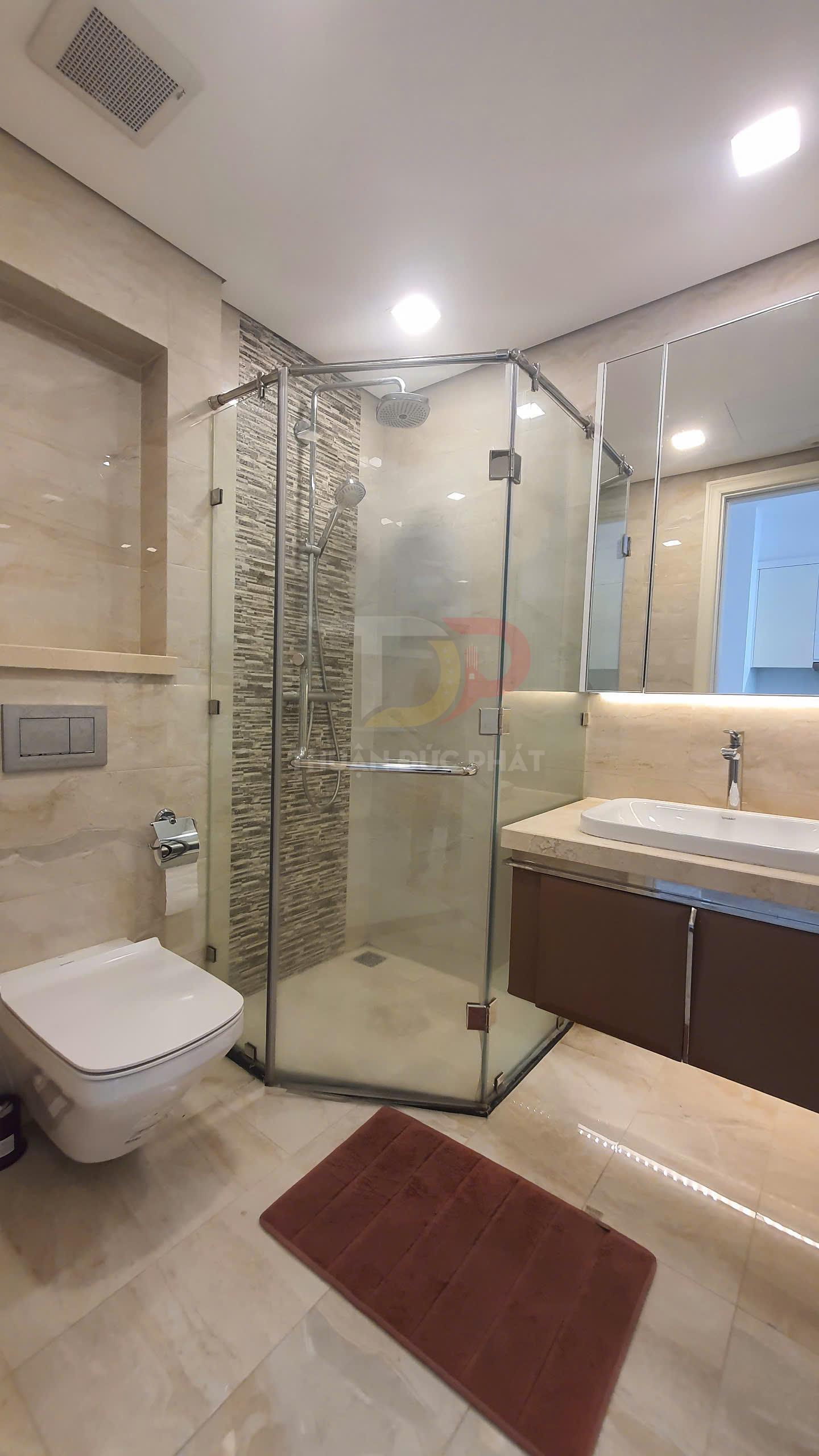 Phòng tắm hiện đại với buồng tắm kính, vòi sen treo tường, bồn cầu treo và lavabo đá sang trọng