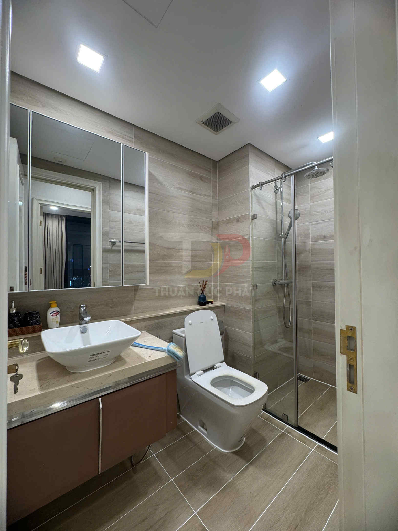 Phòng tắm hiện đại với bồn rửa mặt sứ, bồn cầu và buồng tắm kính lát gạch giả gỗ