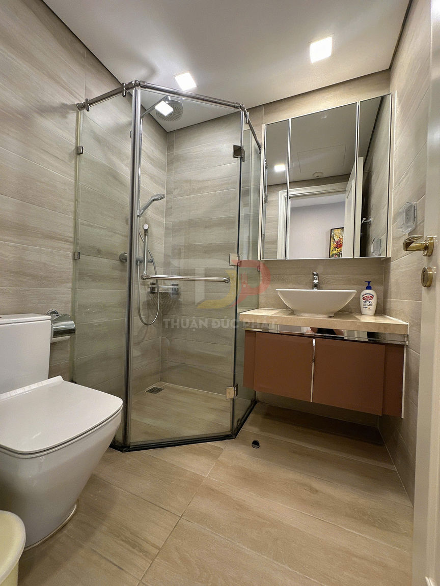 Phòng tắm hiện đại với buồng tắm kính, bồn cầu sứ trắng và lavabo đặt trên tủ gỗ treo tường