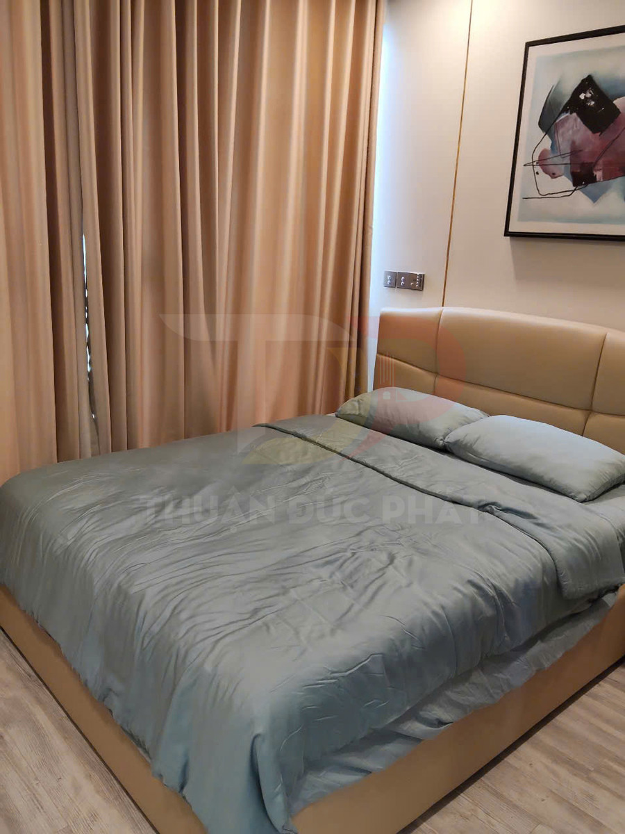 Giường ngủ bọc da màu be với chăn ga gối màu xanh pastel trong phòng ngủ hiện đại có rèm và tranh treo tường