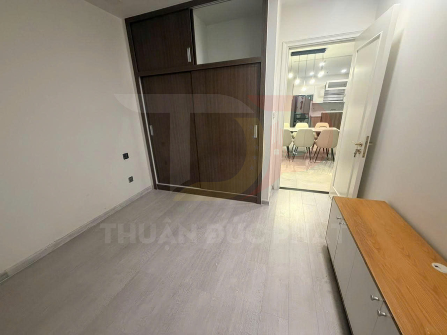 Phòng ngủ nhỏ với tủ quần áo cửa lùa gỗ, sàn gỗ sáng màu nhìn ra khu bếp và bàn ăn hiện đại
