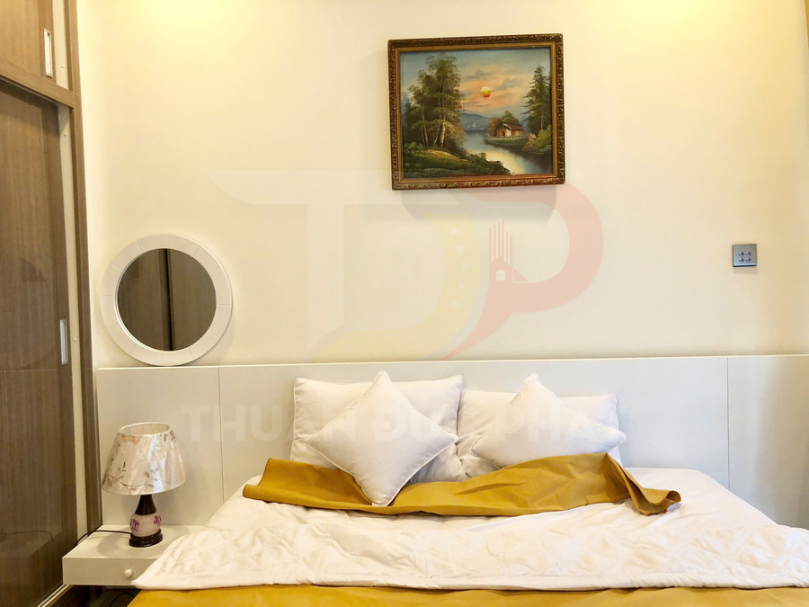 Giường ngủ đôi với chăn ga gối màu trắng vàng và đèn ngủ đặt trên táp đầu giường
