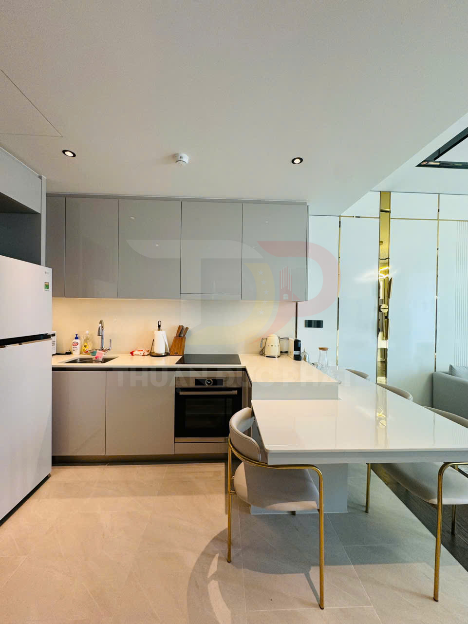 Gian bếp hiện đại với tủ bếp màu xám, bếp từ, lò nướng, tủ lạnh và bàn ăn mặt đá trắng