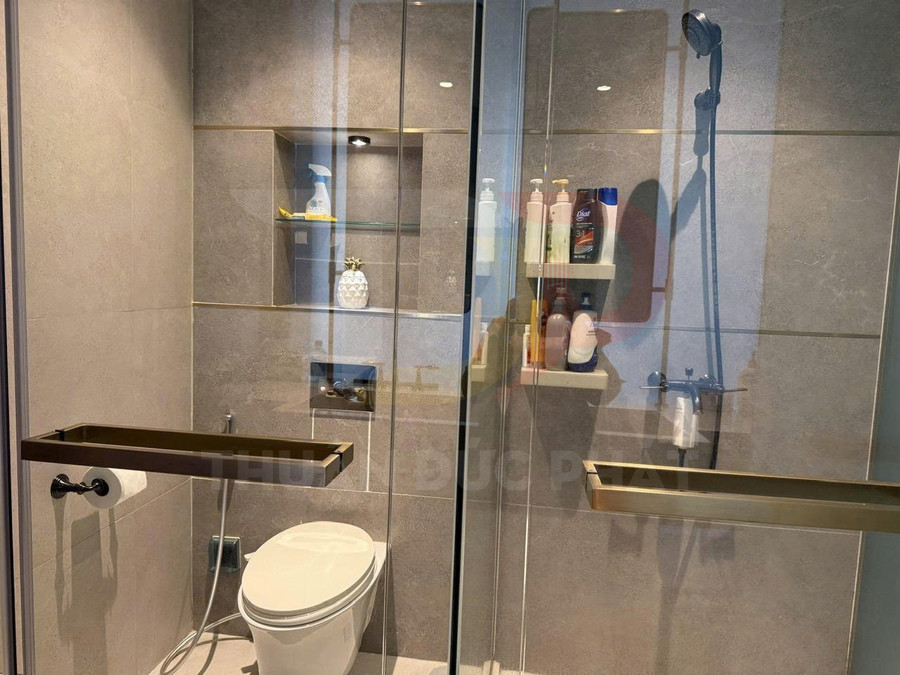 Phòng tắm kính hiện đại với bồn cầu, vòi sen treo tường và kệ đựng đồ vệ sinh gắn tường