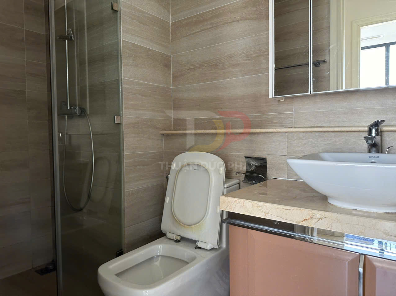 Bồn cầu và lavabo phòng tắm hiện đại cạnh buồng tắm kính, nội thất ốp gạch màu be