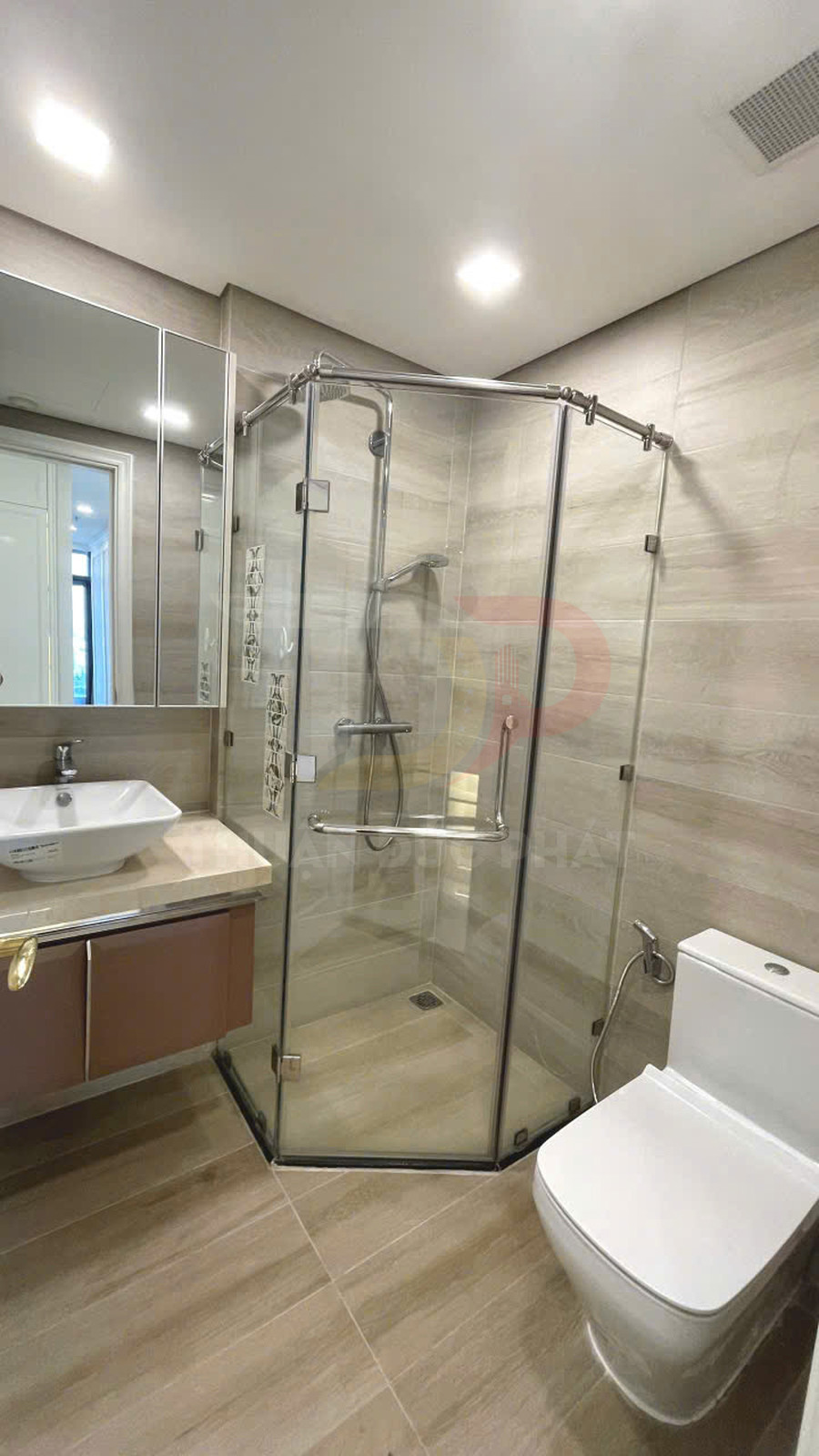Phòng tắm hiện đại với buồng tắm kính góc, vòi sen inox, bồn cầu và lavabo đặt trên tủ gỗ