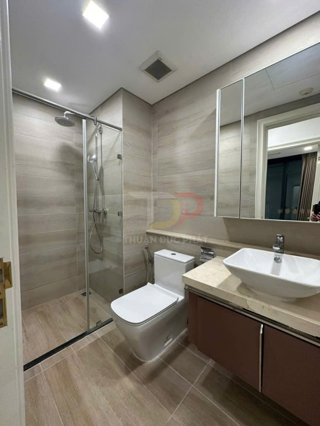 Phòng tắm hiện đại với buồng tắm kính, bồn cầu sứ trắng và lavabo đặt trên tủ gỗ