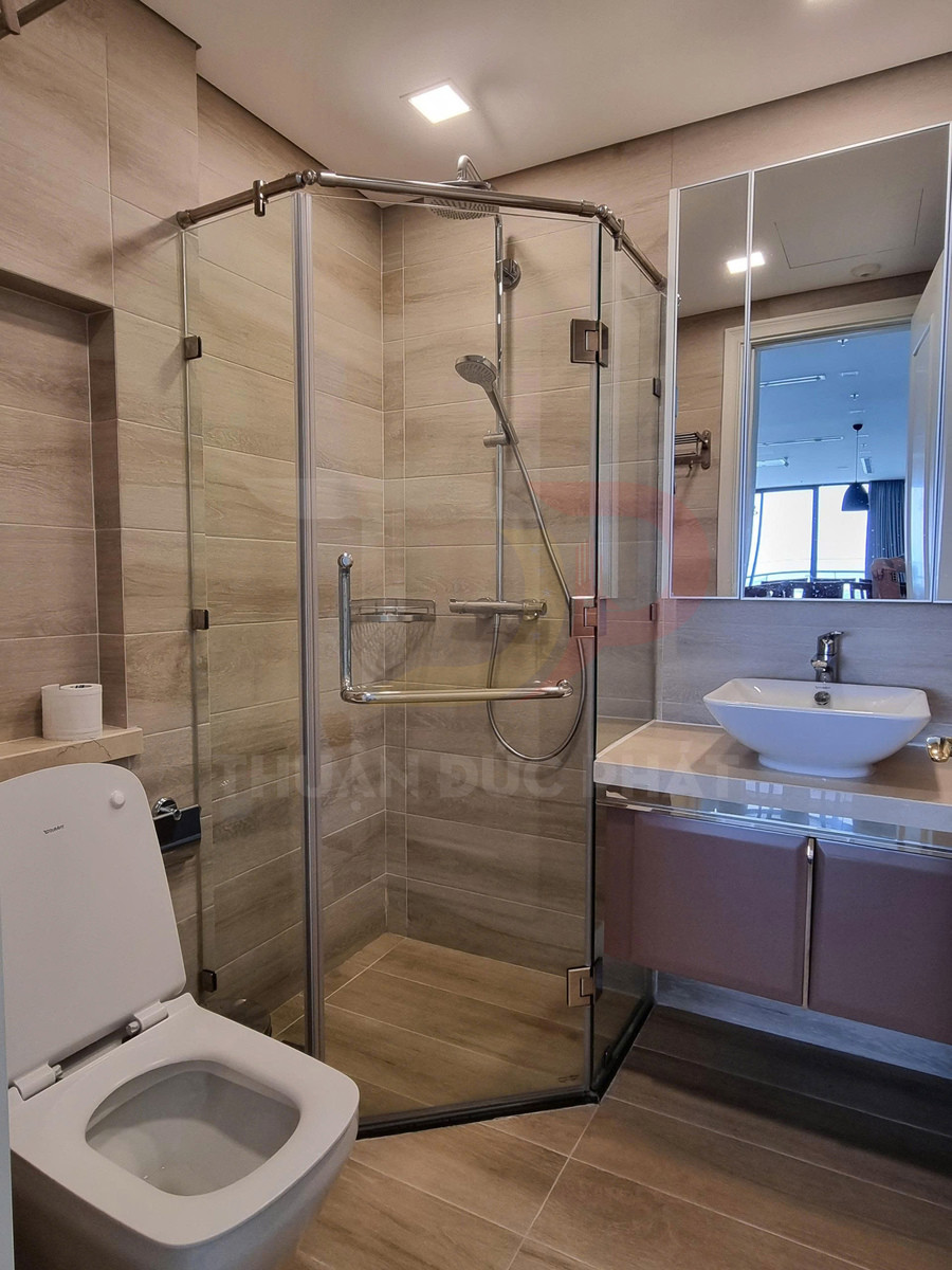 Phòng tắm hiện đại với buồng tắm kính góc, vòi sen inox, bồn cầu và lavabo đặt trên tủ gỗ