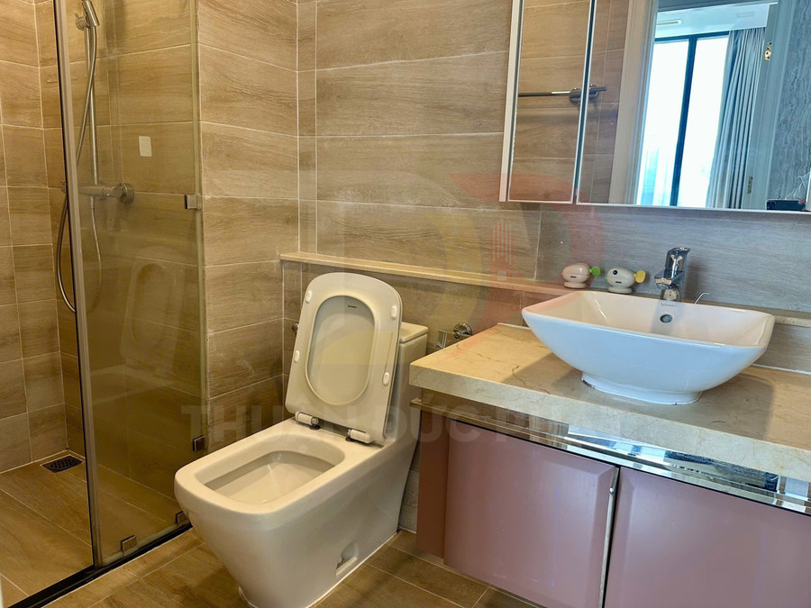Bồn cầu và lavabo sứ trắng trong phòng tắm hiện đại có buồng tắm kính và gạch ốp tường màu be