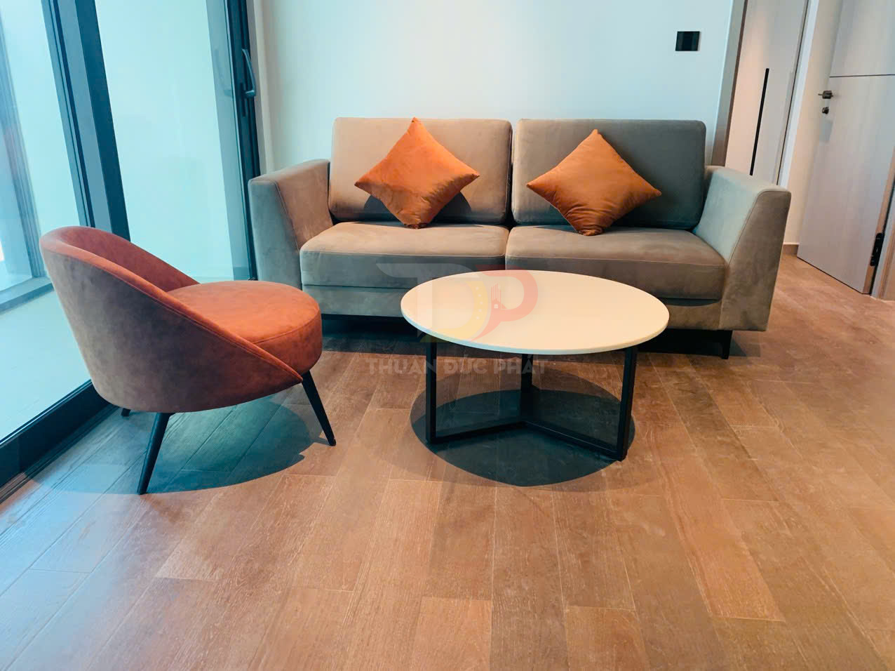 Bộ sofa phòng khách hiện đại với ghế bành nâu, sofa xám và bàn trà tròn mặt trắng chân đen