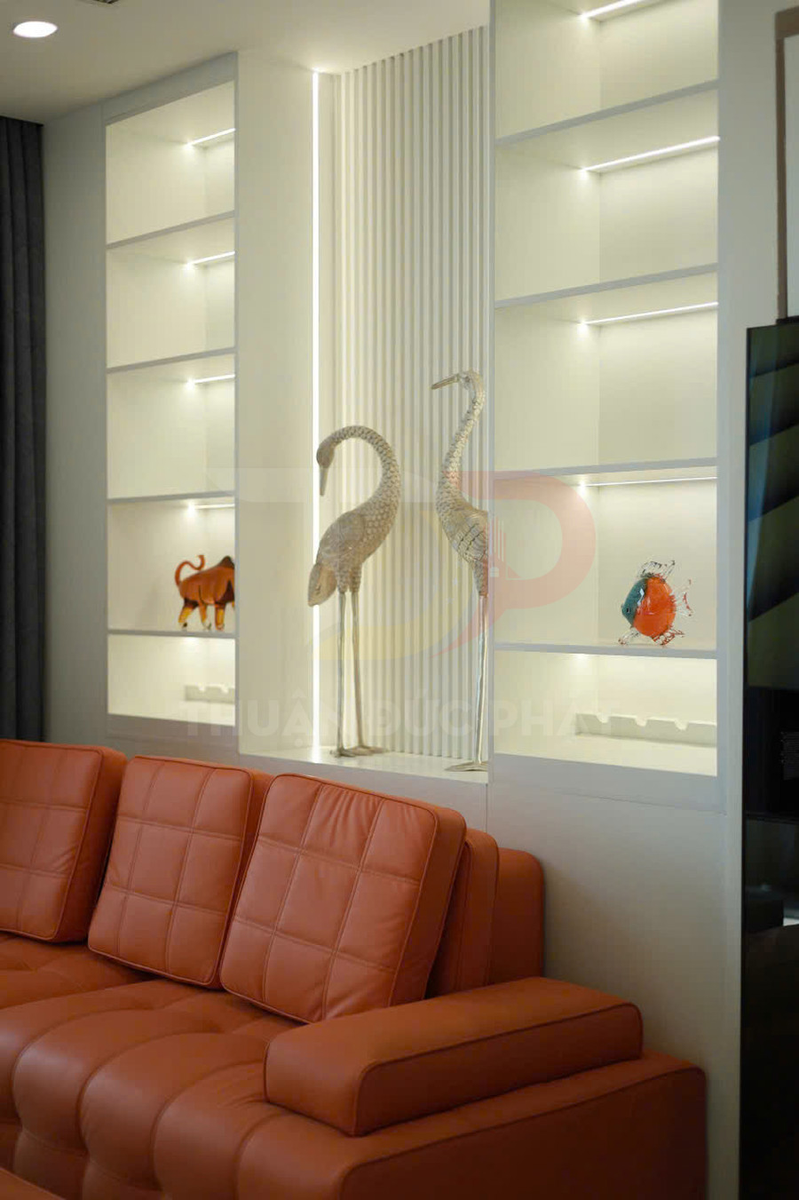 Kệ trang trí phòng khách hiện đại với đèn led âm trần và sofa da màu cam nổi bật