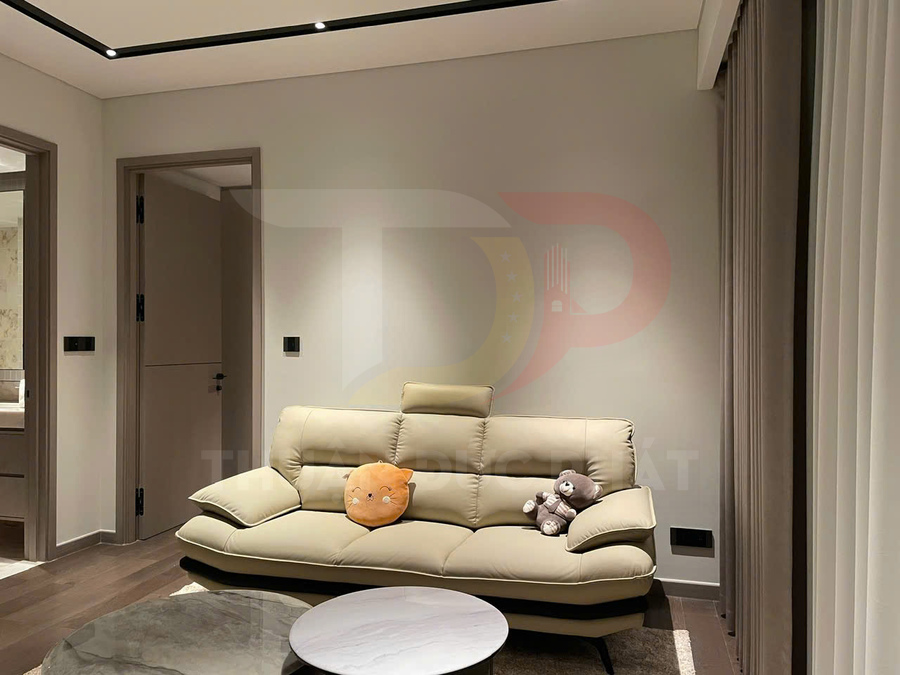Sofa da màu kem hiện đại trong phòng khách nhỏ với gối ôm hình thú và gấu bông trên ghế