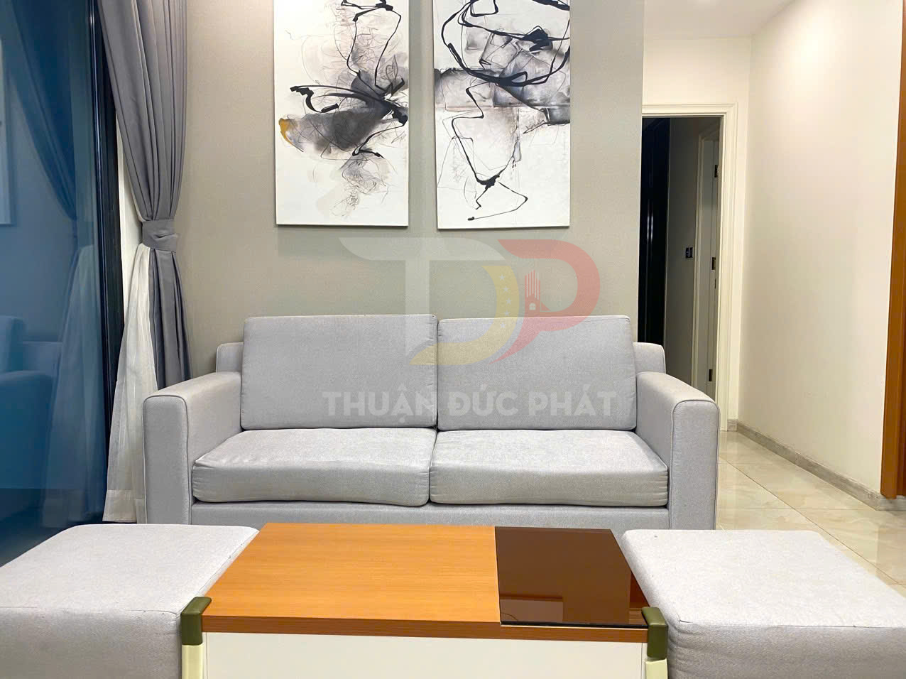Sofa vải màu xám hiện đại kèm bàn trà gỗ và hai tranh treo tường trừu tượng trong phòng khách