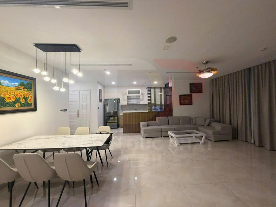 Phòng khách căn hộ hiện đại với sofa góc xám, bàn trà trắng và khu bếp liền kề sáng đèn