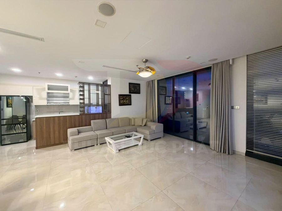 Phòng khách căn hộ hiện đại với sofa góc màu be, bàn trà trắng và bếp mở liền kề