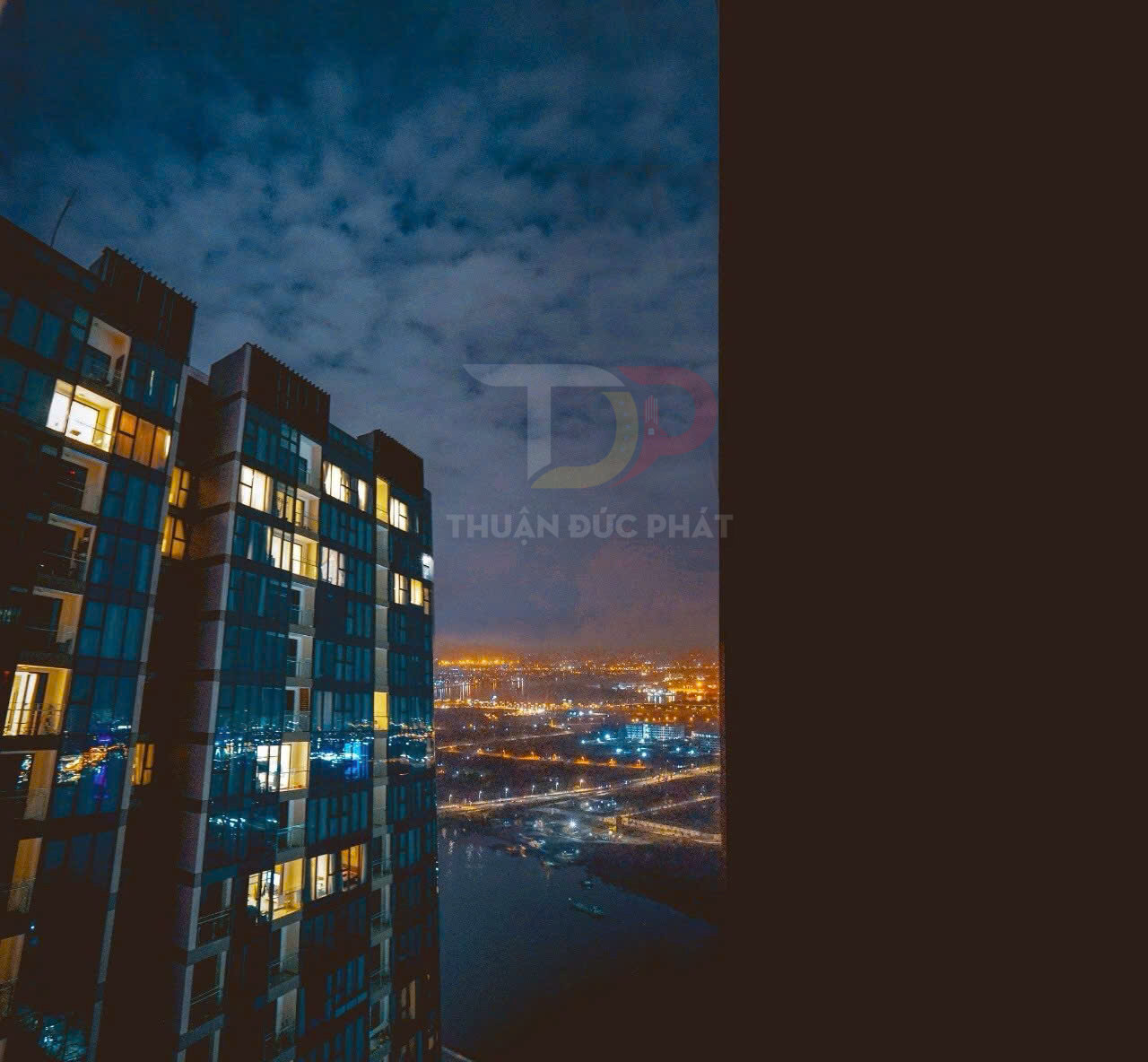 Căn hộ chung cư cao tầng với cửa kính sáng đèn nhìn ra thành phố và sông về đêm