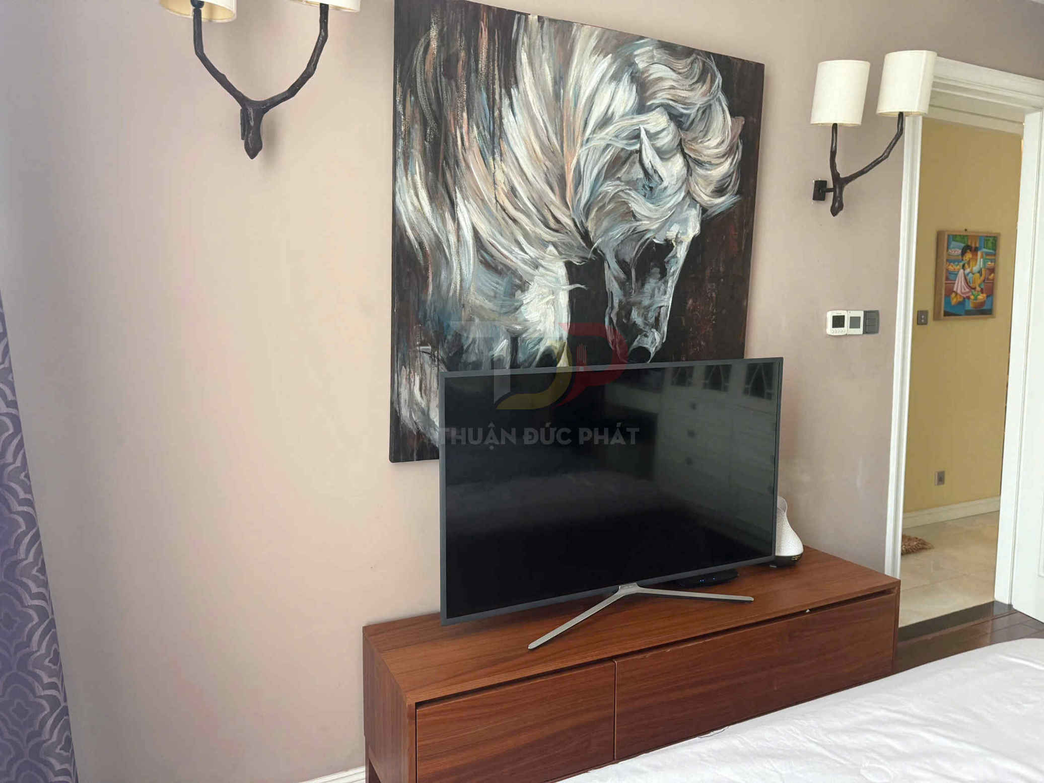 Tivi màn hình phẳng đặt trên kệ gỗ trong phòng ngủ, phía sau là tranh vẽ đầu ngựa trắng