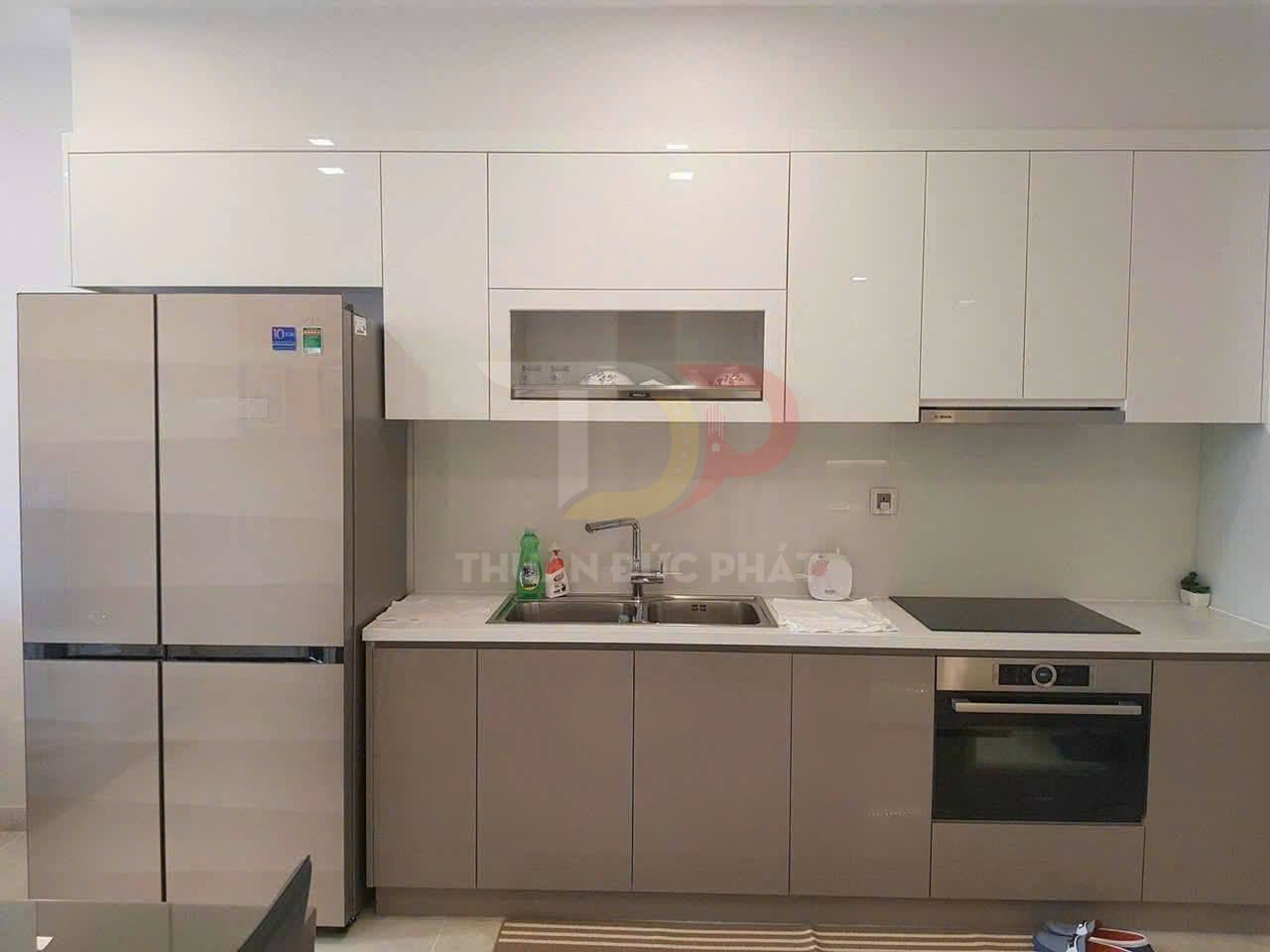 Tủ bếp hiện đại với tủ lạnh lớn, bồn rửa inox, bếp từ và lò nướng âm tủ màu trắng be
