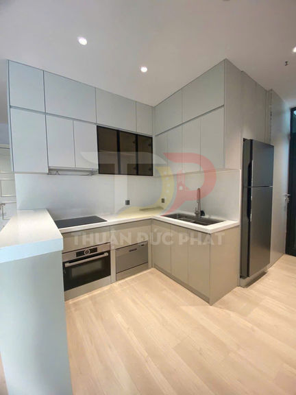 Tủ bếp chữ L hiện đại màu xám với bếp từ, lò nướng âm tủ và tủ lạnh hai cánh trong căn hộ nhỏ gọn