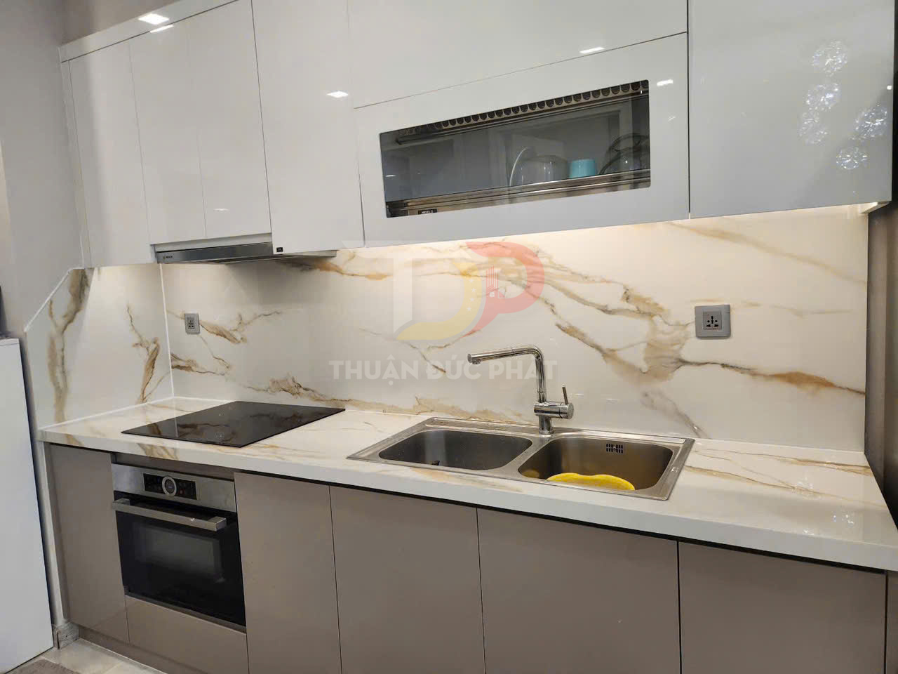 Bếp hiện đại với tủ bếp trắng, mặt đá vân mây, bếp từ âm và chậu rửa inox đôi