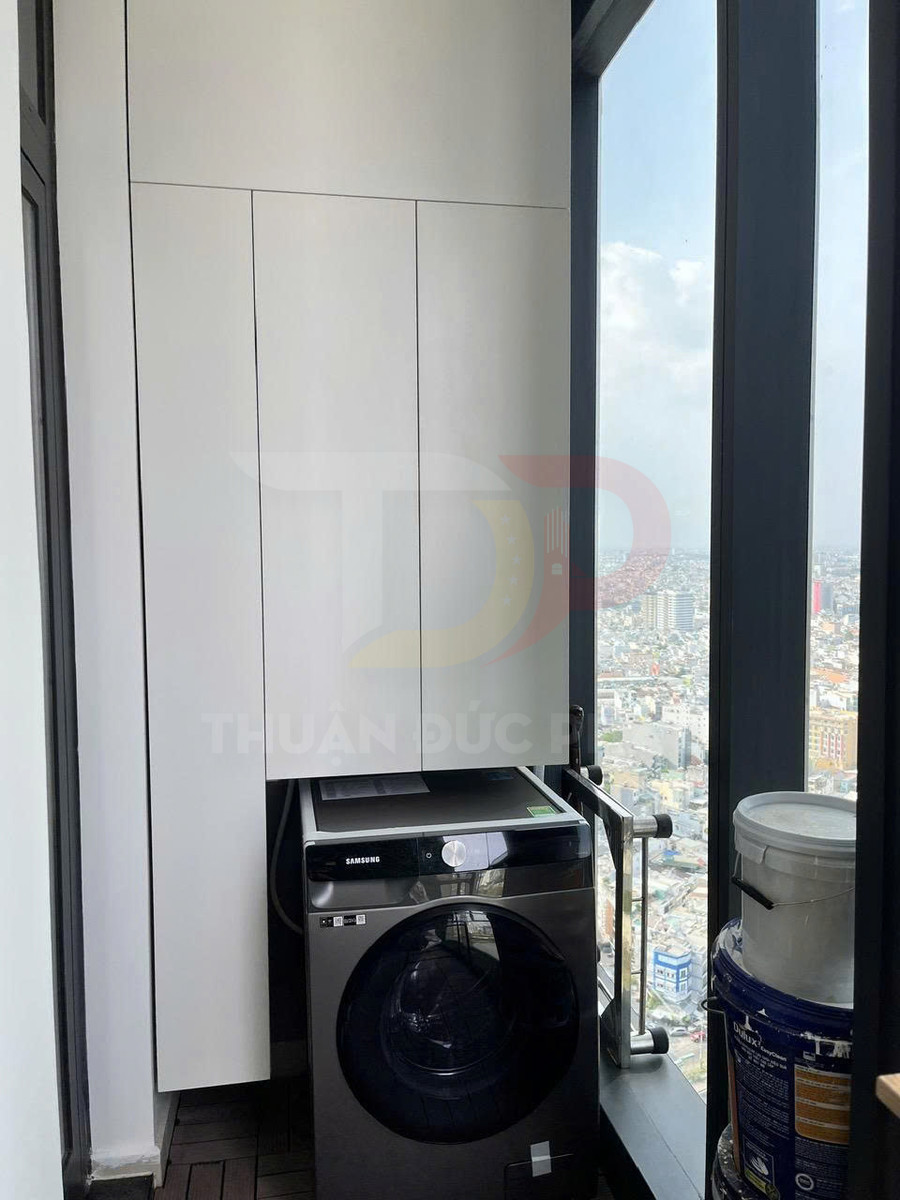 Máy giặt Samsung đặt dưới tủ gỗ âm tường cạnh cửa sổ kính lớn trong căn hộ cao tầng
