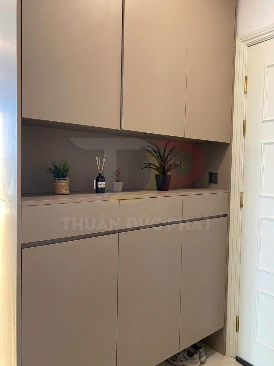 Tủ giày âm tường màu be hiện đại với kệ trang trí chậu cây và lọ tinh dầu cạnh cửa ra vào