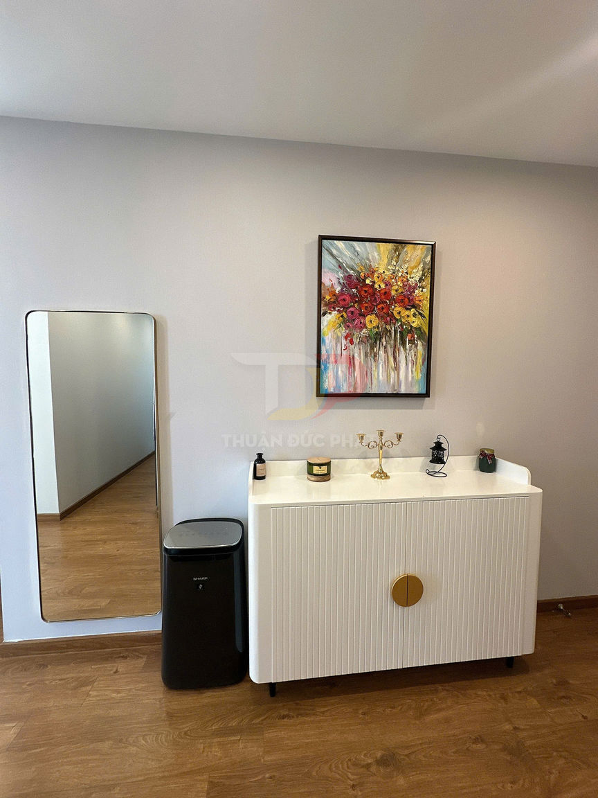 Tủ trang trí màu trắng hiện đại đặt cạnh thùng rác Sharp và gương đứng trong phòng khách sàn gỗ