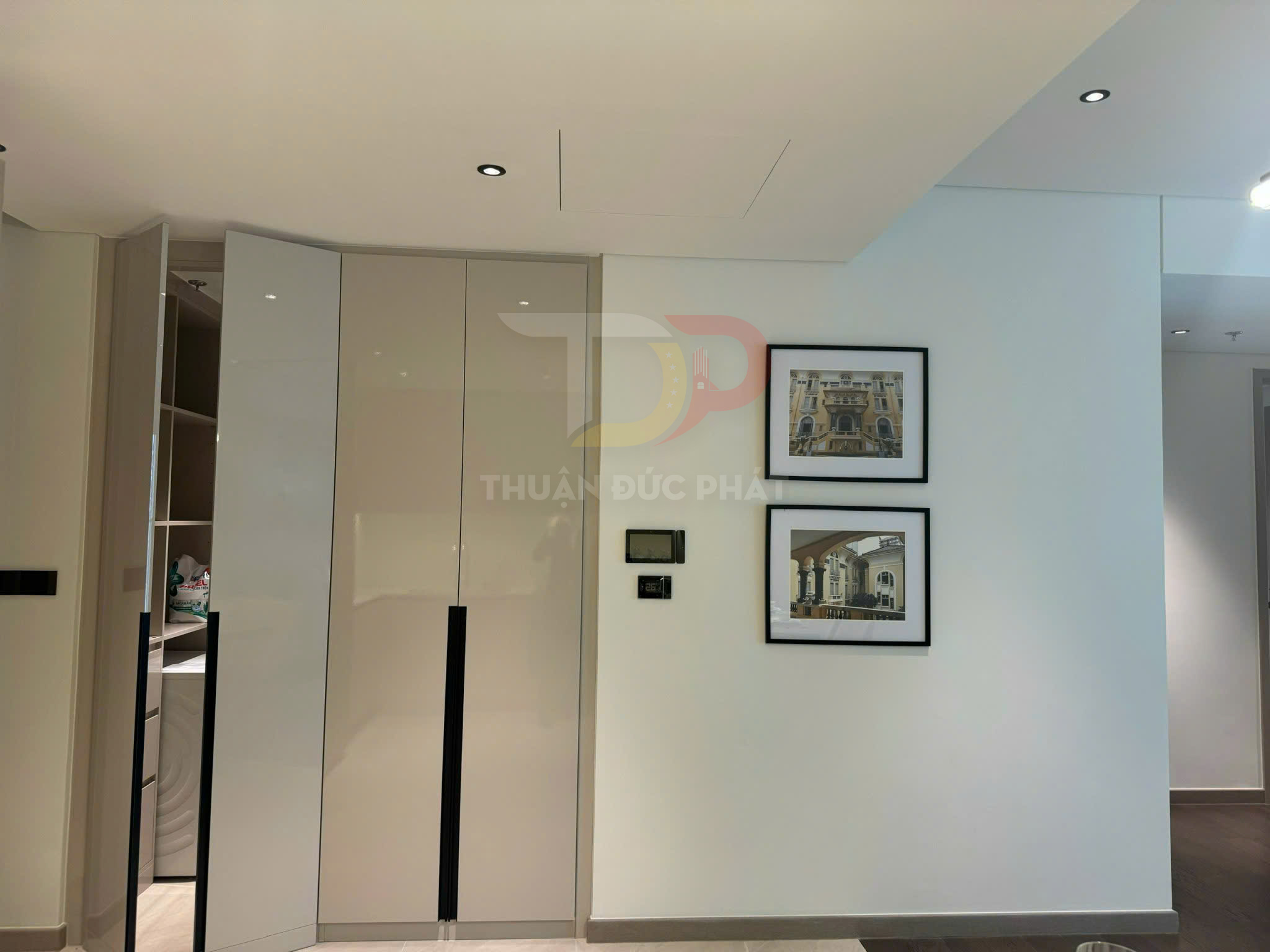 Tủ quần áo âm tường cửa mở trượt màu kem trong phòng ngủ hiện đại, cạnh tường treo hai tranh kiến trúc