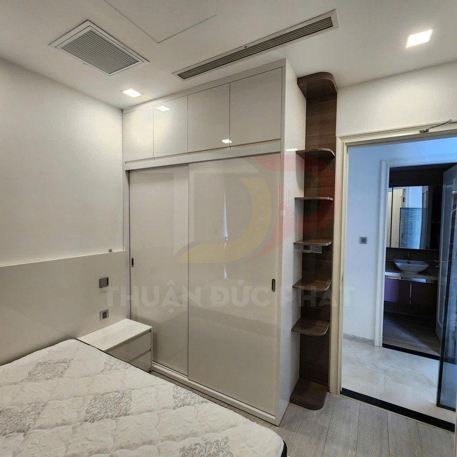 Tủ quần áo âm tường cửa lùa màu trắng hiện đại trong phòng ngủ nhỏ có giường và kệ gỗ cạnh cửa ra vào