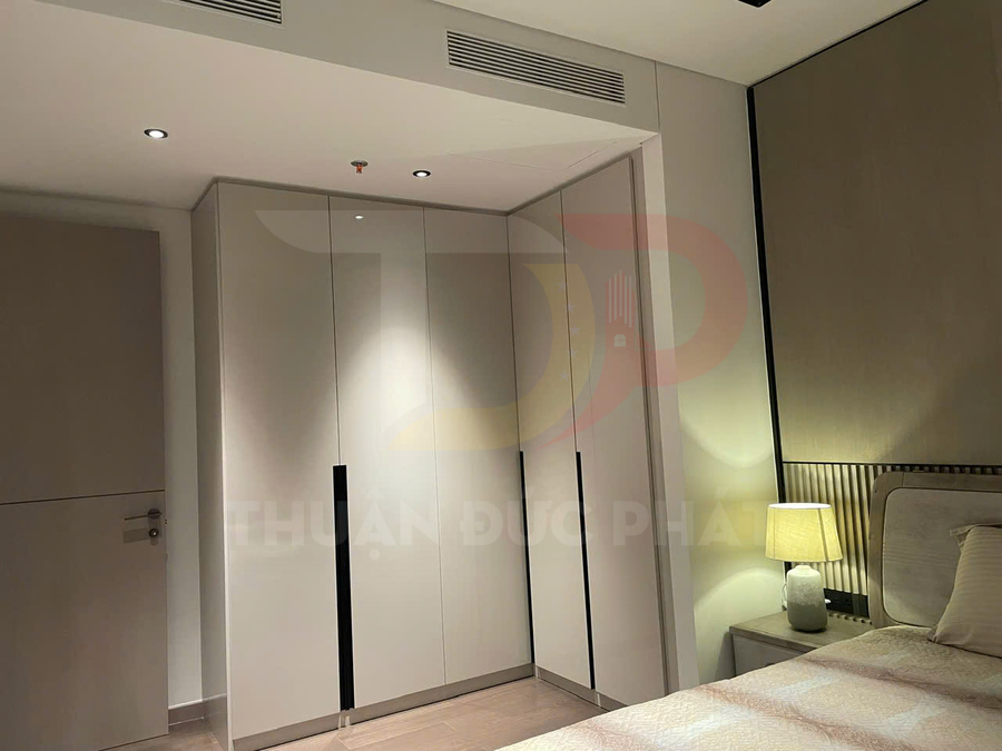 Tủ quần áo âm tường góc chữ L màu trắng trong phòng ngủ hiện đại có giường và đèn ngủ