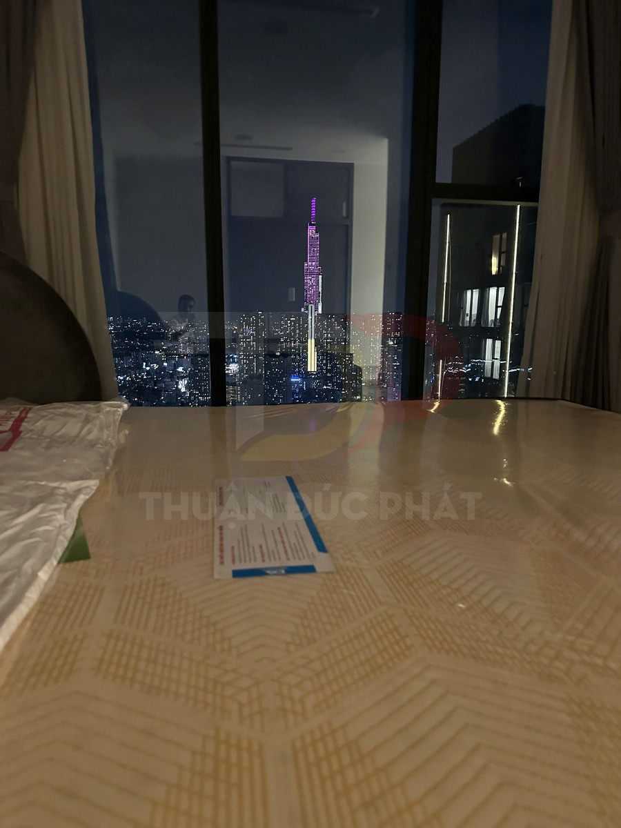 Bàn gỗ trong căn hộ nhìn ra tòa nhà Landmark 81 sáng đèn về đêm qua cửa kính