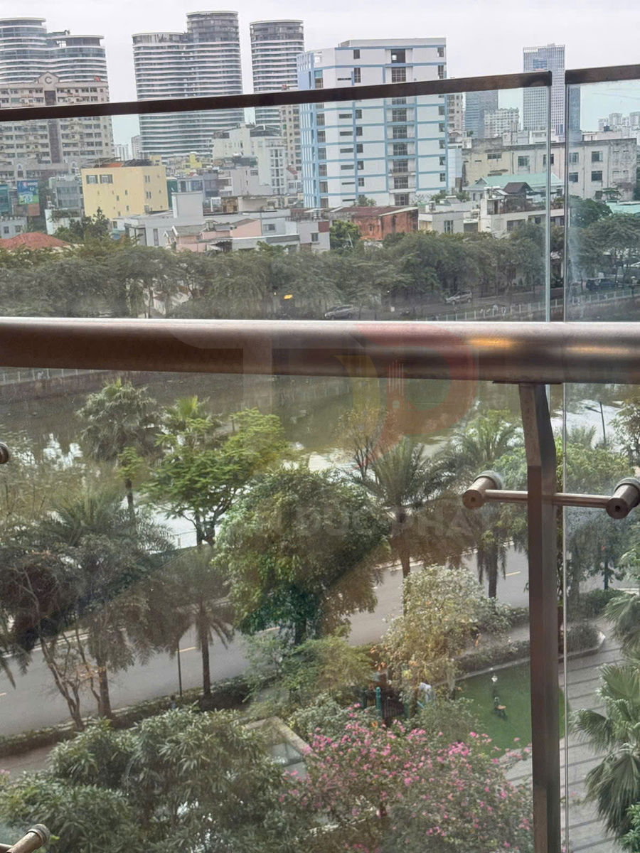 Lan can kính ban công với tay vịn kim loại nhìn ra công viên cây xanh và hồ nước trong khu đô thị